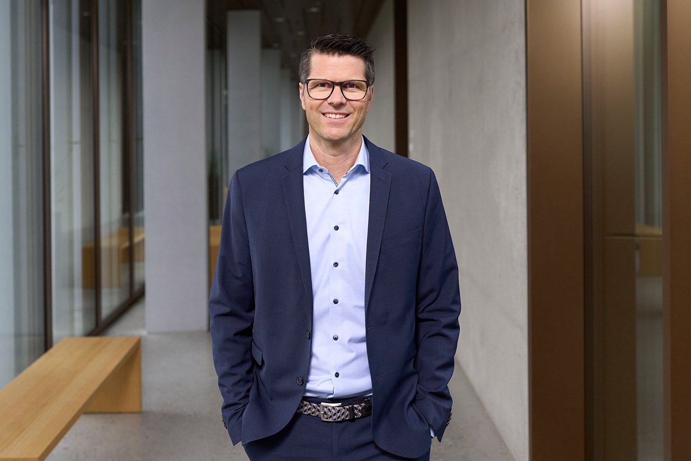 Thomas Jakob, Leiter Sustainability bei PostFinance und verantwortlich für die Nachhaltigkeit, steht lächelnd in einem modernen Bürogebäude. 