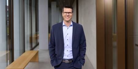 Thomas Jakob, responsable Sustainability chez PostFinance et responsable de la durabilité, se tient en souriant dans un immeuble de bureaux moderne.